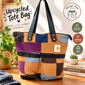 Op de afbeelding: Een patchwork tote bag gemaakt van diverse stoffen vierkanten in tinten paars, bruin, tan en blauw. De tas heeft zwarte lederen handvatten, een ritssluiting aan de bovenzijde en een wit Carhartt merklabel aan de voorzijde van de tas.