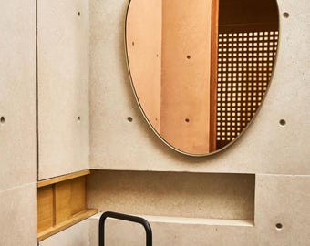 May include: A round mirror with a thin metallic frame mounted on a light gray concrete wall. Below the mirror is a cylindrical concrete sink basin, a tall matte black faucet, and a small black circular handle on the sink surface.