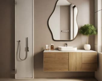 May include: A modern bathroom scene featuring a unique, organic-shaped mirror with a gold frame. The vanity has a wooden cabinet with a white countertop and a white, oval sink. A small potted plant and toiletries are also visible.