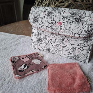 Può includere: Una pochette bianca con un motivo floreale e di volti neri, chiusa con un bottone rosa. Sono presenti anche due accessori rosa abbinati. Uno ha un motivo rosa e bianco, l'altro è in materiale rosa unito e soffice.