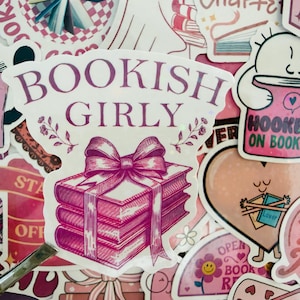May include: A selection of pink and white stickers with book-related designs. One sticker says "Bookish Girly" and features a stack of books tied with a bow. Other stickers include phrases like "Books are better than people" and "Hooked on Books."