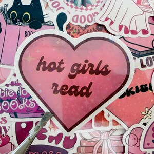May include: A selection of pink stickers with diverse designs and text. A heart-shaped sticker with the words "hot girls read" is prominent. Other stickers include a black cat reading a book, and the text "Barbie do BOOKS".