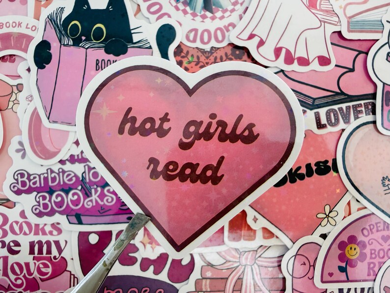 May include: A selection of pink stickers with diverse designs and text. A heart-shaped sticker with the words "hot girls read" is prominent. Other stickers include a black cat reading a book, and the text "Barbie do BOOKS".