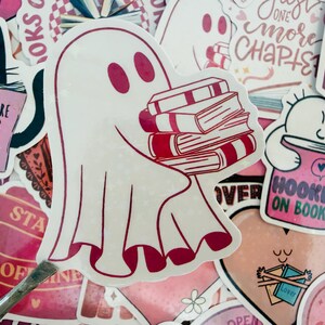 May include: A selection of stickers with a book theme. The main sticker is a white ghost carrying a stack of books with red detailing. Other stickers feature a black cat with a book, and text that says "Books are better than people."
