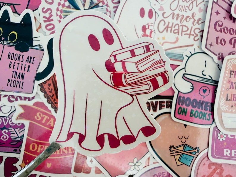 May include: A selection of stickers with a book theme. The main sticker is a white ghost carrying a stack of books with red detailing. Other stickers feature a black cat with a book, and text that says "Books are better than people."
