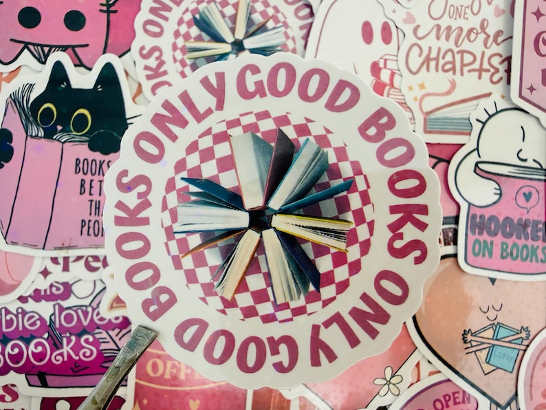 May include: A selection of pink and white stickers with book-related designs. The central sticker says "BOOKS ONLY GOOD BOOKS" around a chequered circle with small book illustrations. Other stickers show a black cat reading and the phrase "Hooked on Books."