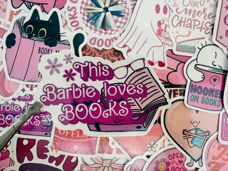 May include: A selection of pink stickers with book-related designs. One sticker says "This Barbie loves BOOKS" with a book and glasses. Other stickers show a black cat reading, a ghost, and the phrase "Hooked on Books."