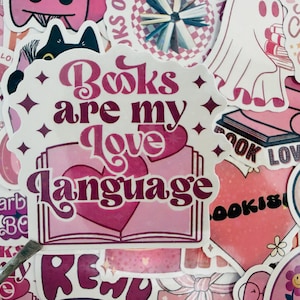 May include: A selection of pink stickers with diverse designs and text. The main sticker says "Books are my Love Language" in a decorative font, featuring a heart and an open book illustration. Other stickers have book-related themes and phrases.