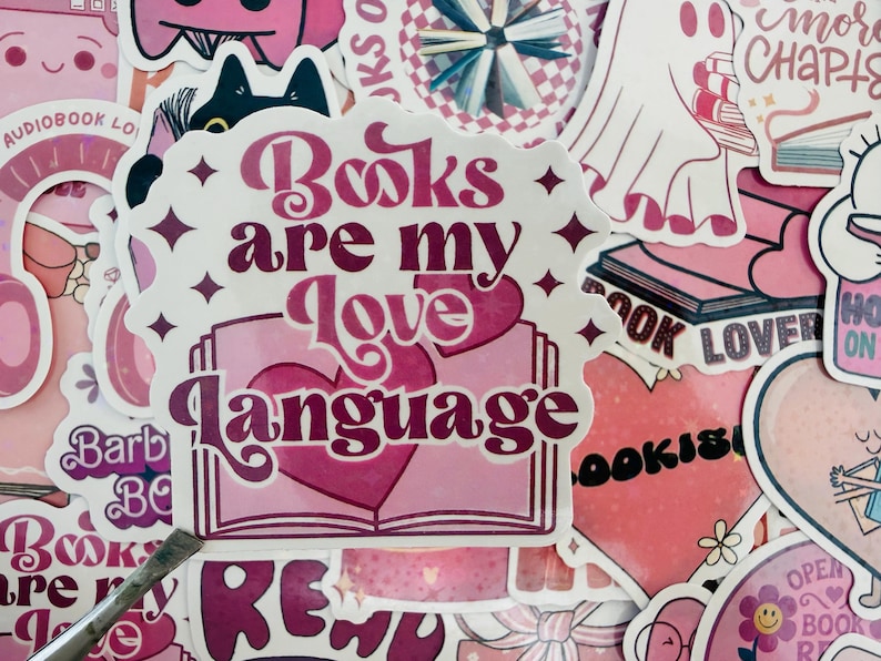 May include: A selection of pink stickers with diverse designs and text. The main sticker says "Books are my Love Language" in a decorative font, featuring a heart and an open book illustration. Other stickers have book-related themes and phrases.