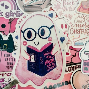 May include: A selection of pink and white stickers with a book theme. The main sticker shows a ghost wearing glasses and reading a book titled "How to Haunt and Be Spooky." Other stickers include a black cat reading, and text that says "Book Lovers."