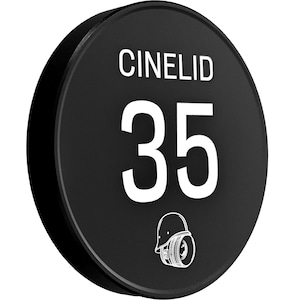 May include: A black, circular Cinelid sign with the number 35 in white. The sign features the word "CINELID" at the top and a camera icon at the bottom. The sign is a solid black color.