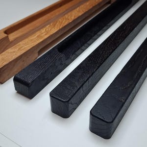 Könnte beinhalten: Nahaufnahme von vier Holzstücken. Zwei sind in einem natürlichen hellbraunen Farbton gehalten, zwei sind schwarz. Alle Teile sind rechteckig mit einer Nut in der Oberseite. Die Holzmaserung ist auf den schwarzen Teilen sichtbar. Wahrscheinlich Bestandteile eines größeren Artikels.