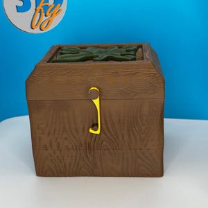 May include: A brown wooden treasure chest with a yellow clasp. The chest has a wood grain texture and a green leaf design on the top. The logo "3D by" is in the upper left corner.
