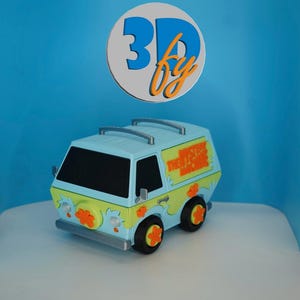 May include: A light blue toy van with green accents, orange flower decals, and a roof rack. The side features the text THE MYSTERY MACHINE in orange. The van has black windows, black wheels with orange flower centers, and a spare tire on the front.