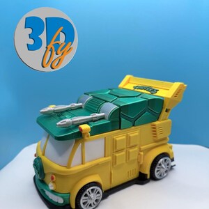 Pode incluir: Uma carrinha de brinquedo amarela e verde com detalhes prateados, semelhante ao ve&iacute;culo das Tartarugas Ninja. A carrinha tem um tejadilho verde, uma carro&ccedil;aria amarela e a palavra "Turtles" no spoiler. A imagem tamb&eacute;m inclui um log&oacute;tipo que diz "3D by".