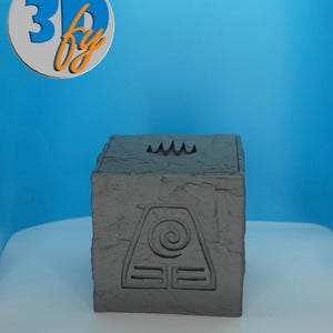 May include: A gray, cube-shaped box with a textured surface and a carved symbol on the front. The top of the box has a wave-like design. The logo "3D by" is in the upper left corner.
