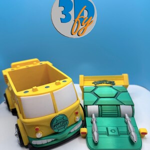 Pode incluir: Dois ve&iacute;culos de brinquedo impressos em 3D: um caminh&atilde;o amarelo e verde com texto "Turtles" e um carro verde com aerof&oacute;lio amarelo. O caminh&atilde;o tem um design de rosto sorridente. O fundo &eacute; um gradiente de azul.