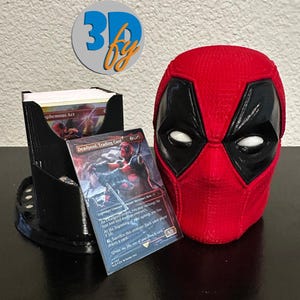 May include: A red and black Deadpool head-shaped card holder and a black card holder with a trading card featuring Deadpool. The card holder is designed to hold trading cards. The logo "3D by" is visible in the background.