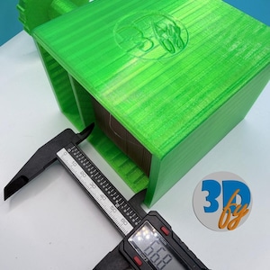 May include: A bright green 3D-printed spool holder with a gear-like handle and a digital caliper measuring 66.8 mm. The holder has a logo on the top. The caliper is black with white markings.