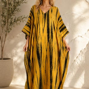 May include: A floor-length kaftan dress featuring a mustard yellow base with vertical black tie-dye stripes. The garment has a V-neckline, wide short sleeves, and a loose, flowing silhouette that extends to the floor, covering the feet completely.