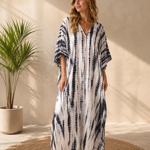 May include: A floor-length kaftan dress featuring a V-neckline and wide, loose sleeves. The garment is decorated with a vertical tie-dye pattern in dark charcoal grey and white, with side slits extending from the hemline up to the mid-thigh.