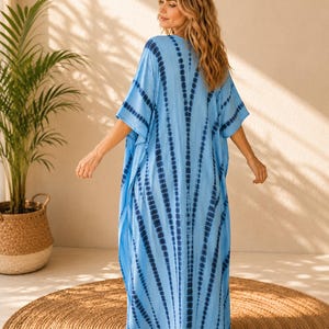 May include: A floor-length kaftan dress in light blue featuring a dark blue tie-dye pattern with vertical stripes radiating from the center. The garment has wide, loose sleeves and a relaxed, flowing silhouette that reaches down to the ankles.