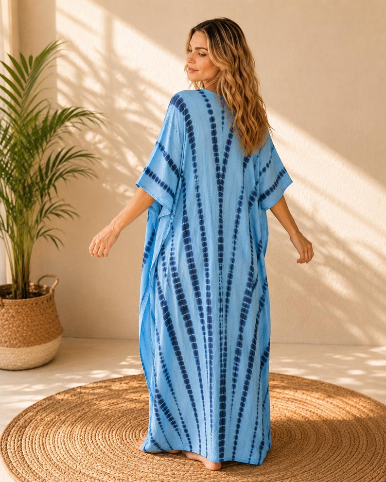 May include: A floor-length kaftan dress in light blue featuring a dark blue tie-dye pattern with vertical stripes radiating from the center. The garment has wide, loose sleeves and a relaxed, flowing silhouette that reaches down to the ankles.