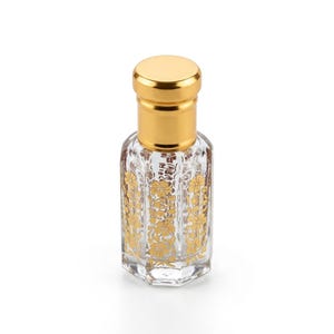 May include: A clear glass perfume bottle with a gold cap and gold floral design. The bottle has an octagonal shape and is filled with a clear liquid. The cap is a solid gold color.