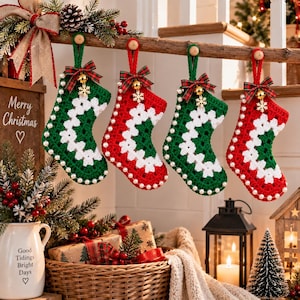Könnte beinhalten: Vier gehäkelte Weihnachtsstrümpfe hängen in einer Reihe, abwechselnd in grünen und roten Hauptfarben mit weißen Granny-Square-Mustern. Jeder Strumpf ist mit einer karierten Schleife, einer goldenen Glocke, einem Schneeflockenanhänger und Perlen verziert.
