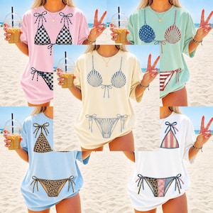 Peut inclure: Une collection de cinq t-shirts à manches courtes de différentes couleurs, dont rose clair, vert clair, crème, bleu clair et blanc. Chaque t-shirt présente une impression graphique d'un ensemble bikini deux pièces avec des motifs variés.
