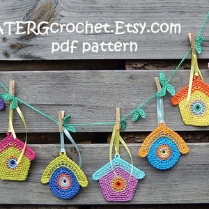 Könnte beinhalten: Eine bunte Häkelgirlande aus Vogelhäuschen hängt an einem Holzzaun. Die Girlande ist aus verschiedenenfarbigen Garnen gefertigt und zeigt eine Vielzahl von Vogelhäuschen-Designs. Der Text "ATERGcrochet.Etsy.com pdf pattern" ist oben im Bild sichtbar.