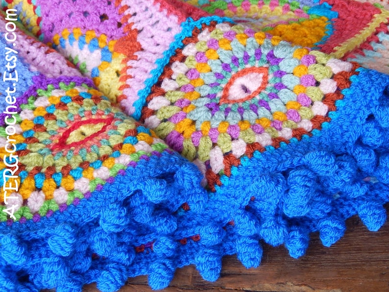 May include: A colorful crocheted blanket with a blue fringe border. The blanket is made up of squares with different patterns and colors, including red, orange, yellow, green, blue, purple, and pink.