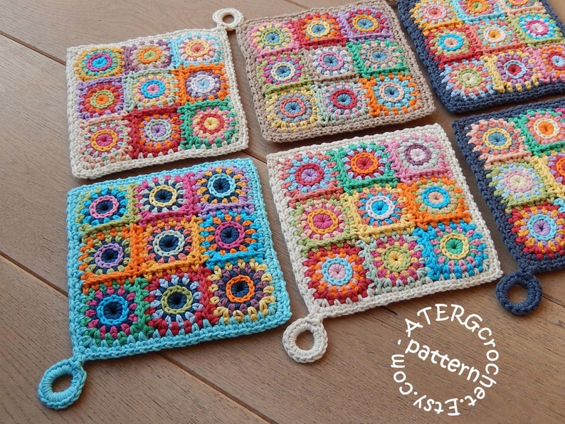 May include: Four crocheted pot holders with colorful square patterns and a loop handle. The pot holders are made with different colored yarns, including blue, green, orange, red, yellow, and brown. The pot holders are arranged in a row on a wooden surface. The text on the bottom right corner of the image reads '#EtsyCroche #ATERGcrochet .pattern.com'. 