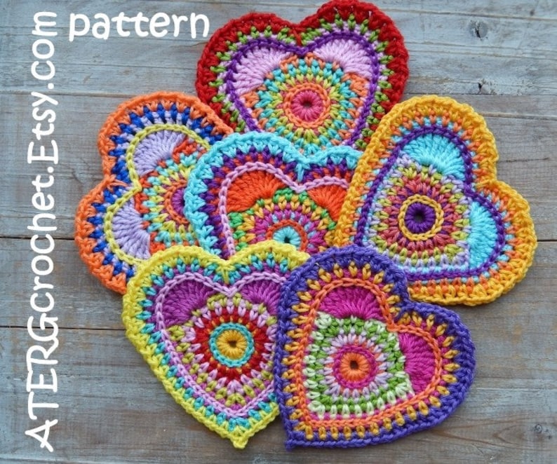 May include: Six colorful crocheted hearts with mandala patterns in shades of pink, orange, yellow, green, blue, and purple. The hearts are arranged in a circle on a wooden surface. The text "ATERcrochet.Etsy.com pattern" is visible in the top left corner of the image.