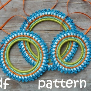 Peut inclure: Trois cerceaux en crochet bleu, vert, blanc et orange. Les cerceaux sont empilés les uns sur les autres. Le texte "pdf pattern" est en bas de l'image.