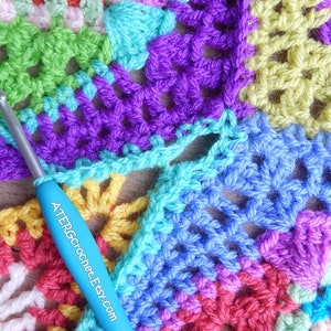 May include: A close-up of a colorful crochet project with a blue crochet hook. The project is made up of squares in various colors, including green, purple, blue, yellow, pink, and red. The crochet hook has the text "ATERGrochet.Etsy.com" printed on it.