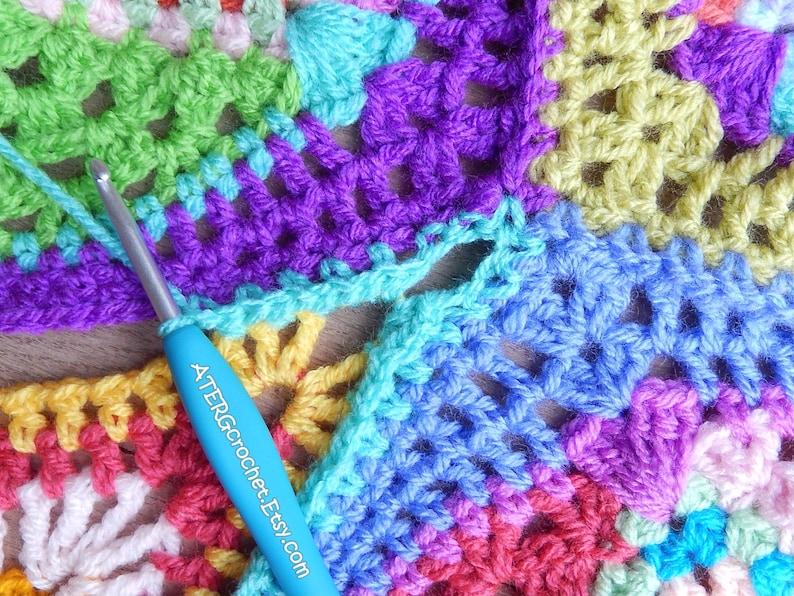 May include: A close-up of a colorful crochet project with a blue crochet hook. The project is made up of squares in various colors, including green, purple, blue, yellow, pink, and red. The crochet hook has the text "ATERGrochet.Etsy.com" printed on it.