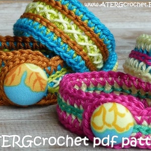May include: Three crocheted bracelets with colourful stripes and fabric buttons. The bracelets are made with different coloured yarns, including turquoise, pink, brown, yellow, and green. The buttons are covered in fabric with a floral pattern.