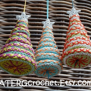May include: Three handmade crochet Christmas tree ornaments. Each tree is cone-shaped, with colorful yarn and a silver star topper. The trees feature various color combinations, including green, pink, and orange. The text "ATERGcrochet.Etsy.com" is at the bottom.