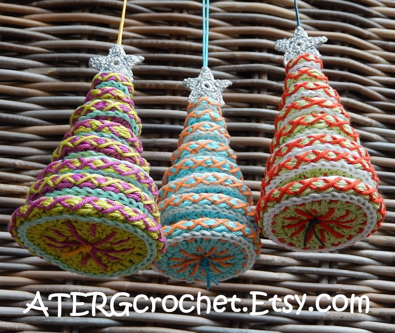 May include: Three handmade crochet Christmas tree ornaments. Each tree is cone-shaped, with colorful yarn and a silver star topper. The trees feature various color combinations, including green, pink, and orange. The text "ATERGcrochet.Etsy.com" is at the bottom.