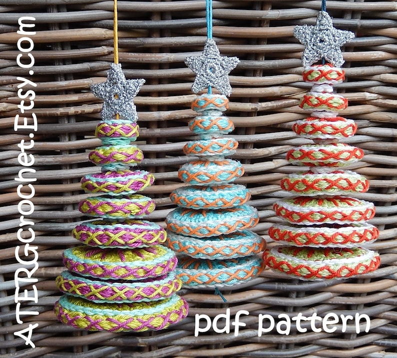 May include: Three handmade crochet Christmas tree ornaments. Each tree is made of stacked, colorful rings with a star on top. The trees are in shades of green, pink, orange, and white. The text "pdf pattern" is visible.