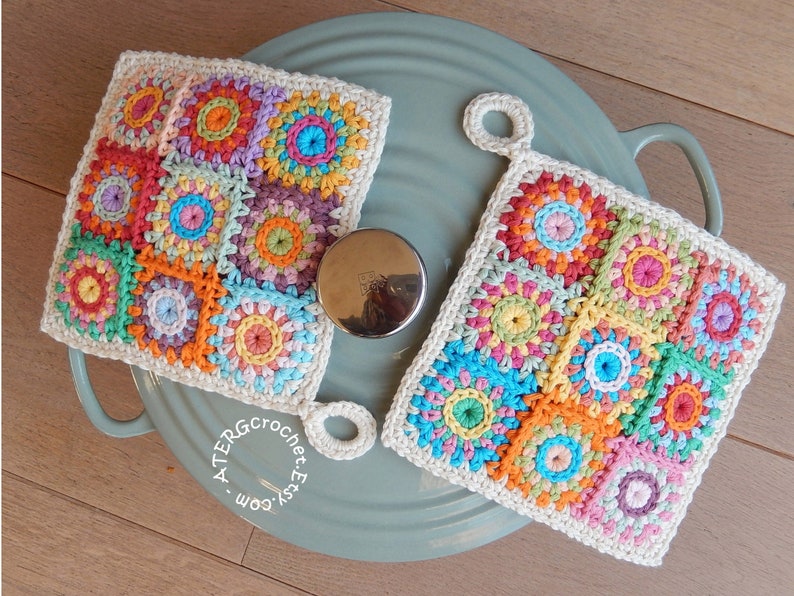 May include: Two crocheted pot holders with a colorful patchwork design. Each pot holder is made of a variety of bright colors, including pink, orange, yellow, green, blue, and purple. The pot holders have a loop for hanging. The text on the pot holder reads 'ATERGcrochet.Etsy.com'.