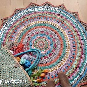 May include: A colorful crochet mandala rug with a starburst border. The rug is made with a variety of colors, including orange, red, yellow, green, blue, and purple. The rug is lying on a wooden floor. A basket, yarn, and flowers are in the foreground.