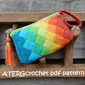 Puede incluir: Una bolsa de crochet arcoíris con un borla verde y naranja. La bolsa tiene un asa y está hecha con un patrón de punto de diamante. Patrón PDF ATERGcrochet.