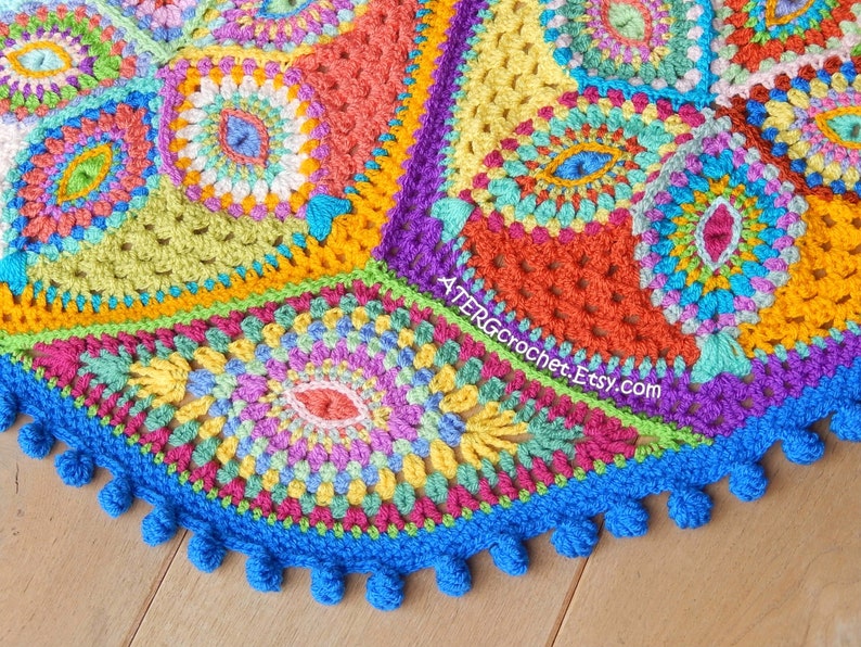 May include: A colorful crocheted round blanket with a blue border and pom-poms. The blanket is made up of different colored squares with intricate patterns.
