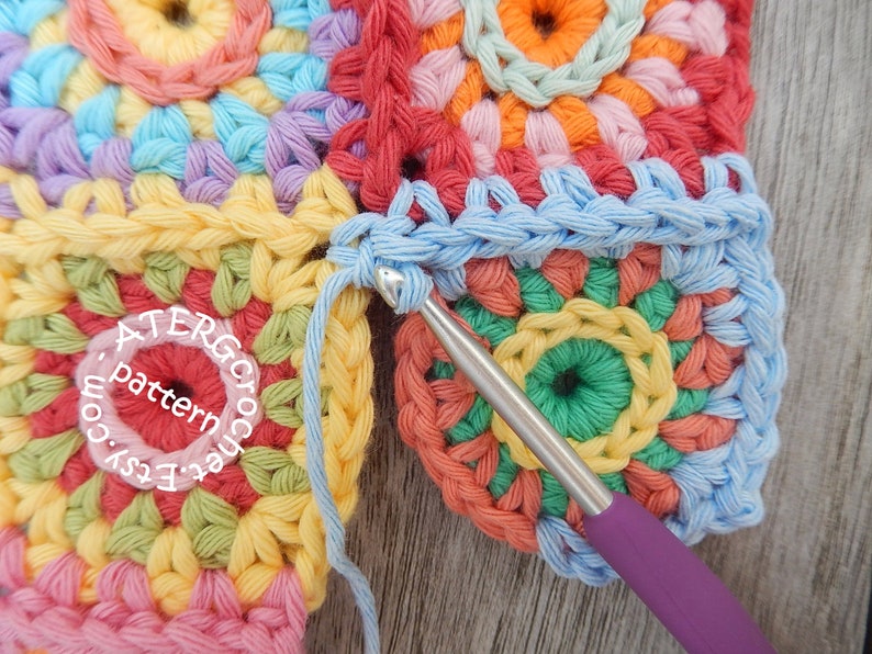 May include: A close-up of a crochet project with a blue crochet hook. The project is made of colorful yarn and has a circular pattern. The text 'ATERGcrochet pattern Easy.com' is visible in the image.