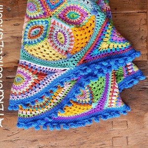 May include: A colorful crocheted blanket with a blue crocheted border and blue pom-poms. The blanket is made up of different geometric shapes and patterns.