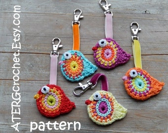 May include: Five crocheted bird keychains in different colors, including pink, blue, yellow, orange, and red. Each bird has a round, colorful center and a white eye. The keychains are attached to colorful ribbon loops.