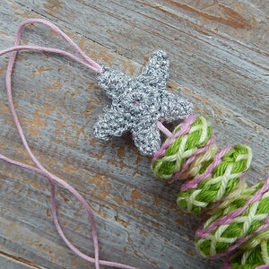May include: A handmade crochet necklace featuring a silver starfish pendant and a series of green, pink, and white woven rings. The necklace is strung on a pink cord. The text "ATERGcrochet.Etsy.com" is visible.