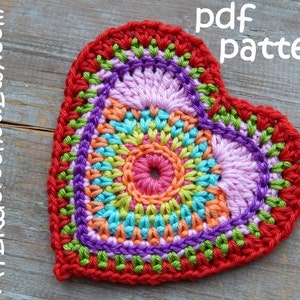May include: A colorful crocheted heart with a multi-colored center and a red border. The heart is on a wooden surface. The text "pdf pattern" is written above the heart. The text "ATERcrochet.Etsy.com" is written to the left of the heart.